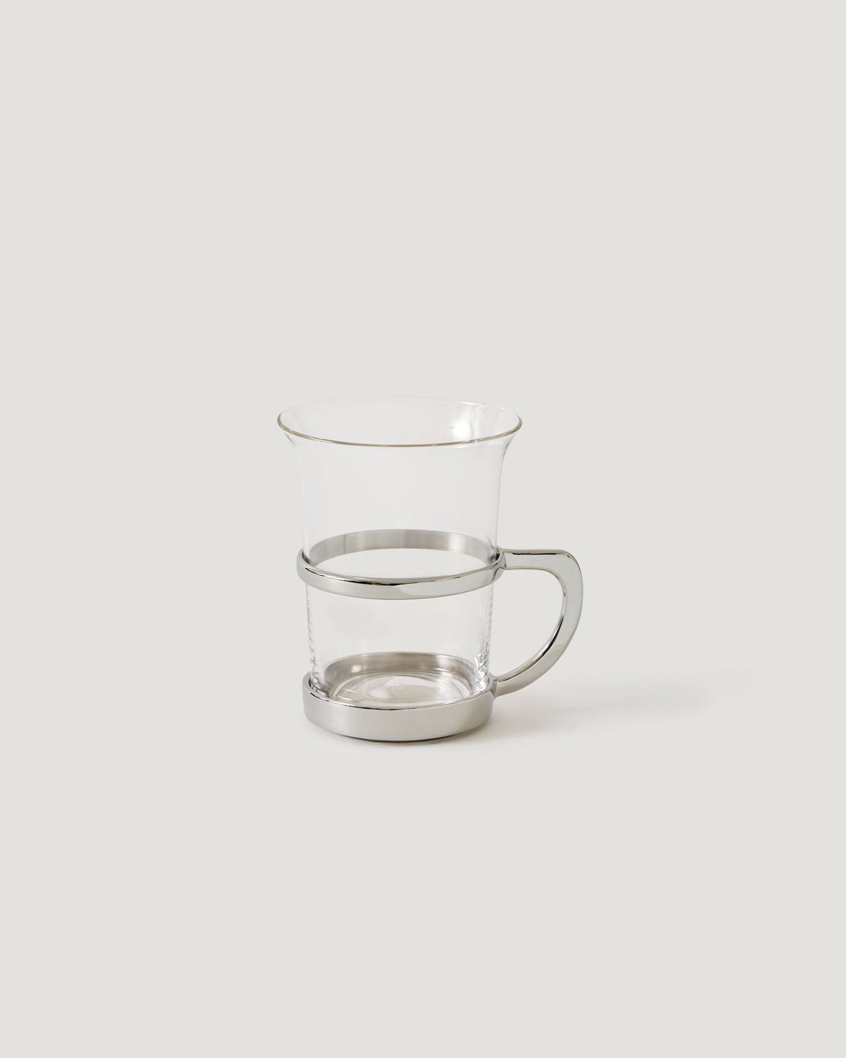A clear glass mug with a polished silver metal band around the middle and a matching silver base, set against a solid light gray background.